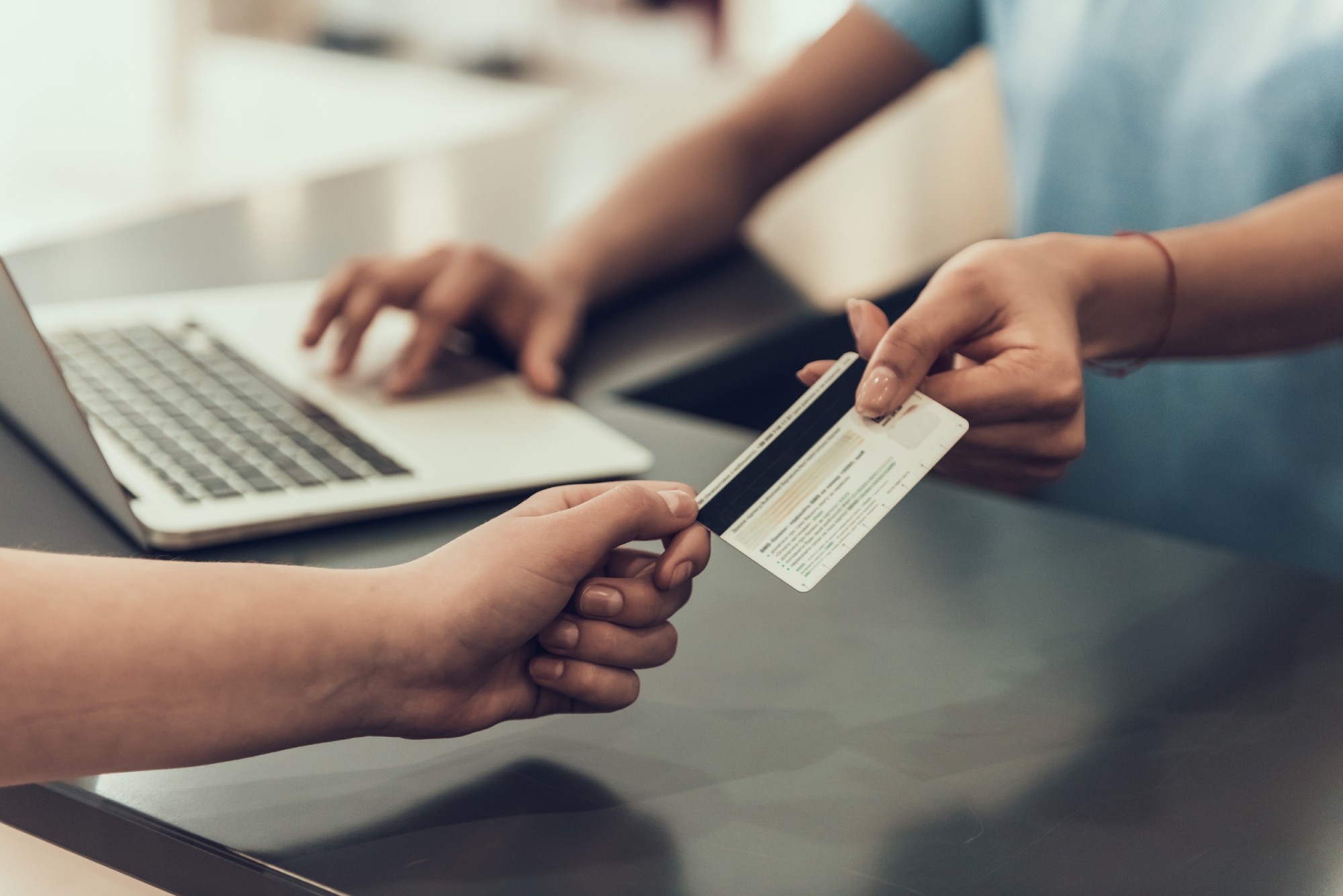 Closeup Customer Paying with Credit Card in Store. Close up of Man giving Credit Card to Young Black Woman using Laptop in Store. Female Employee takes Payment from Male Customer. Shopping Concept