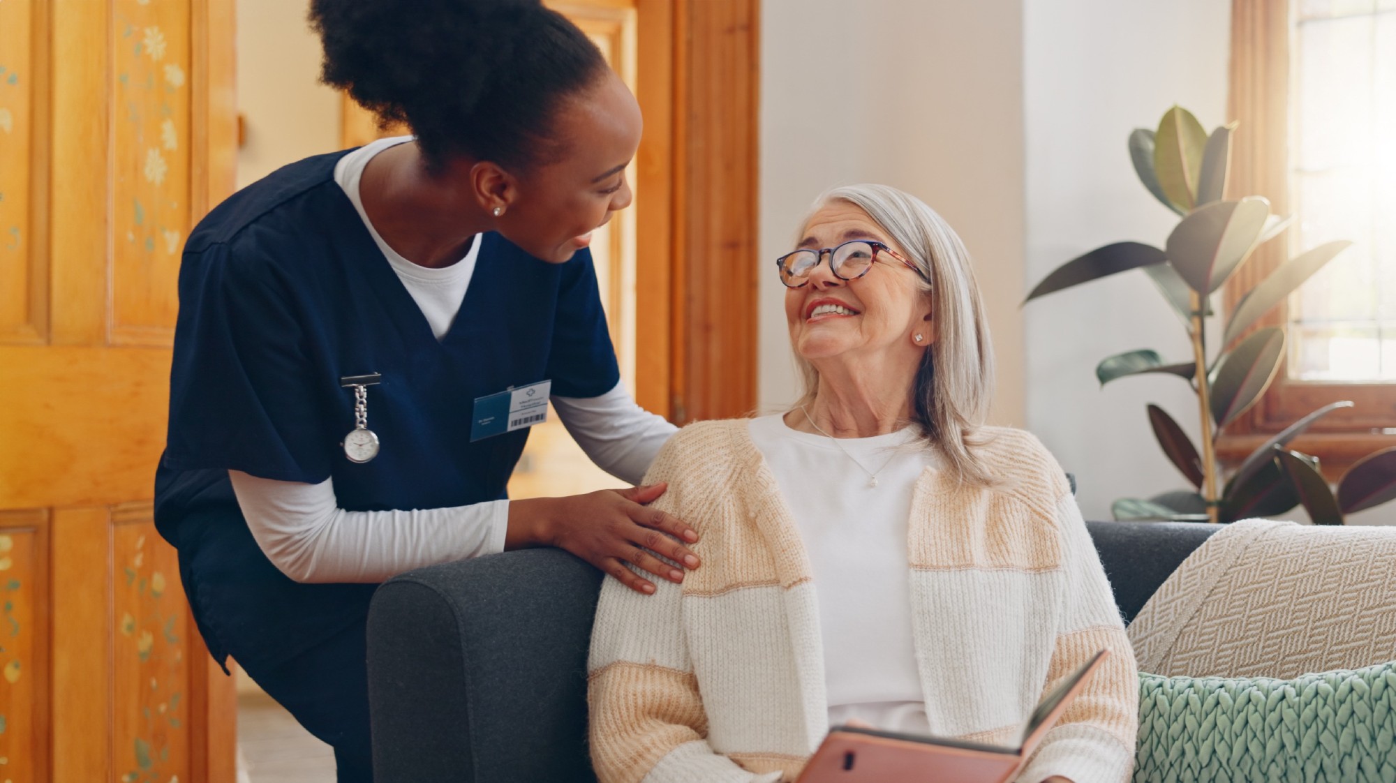 nurse and senior woman on sofa reading notebook for checklist consultation research checkup